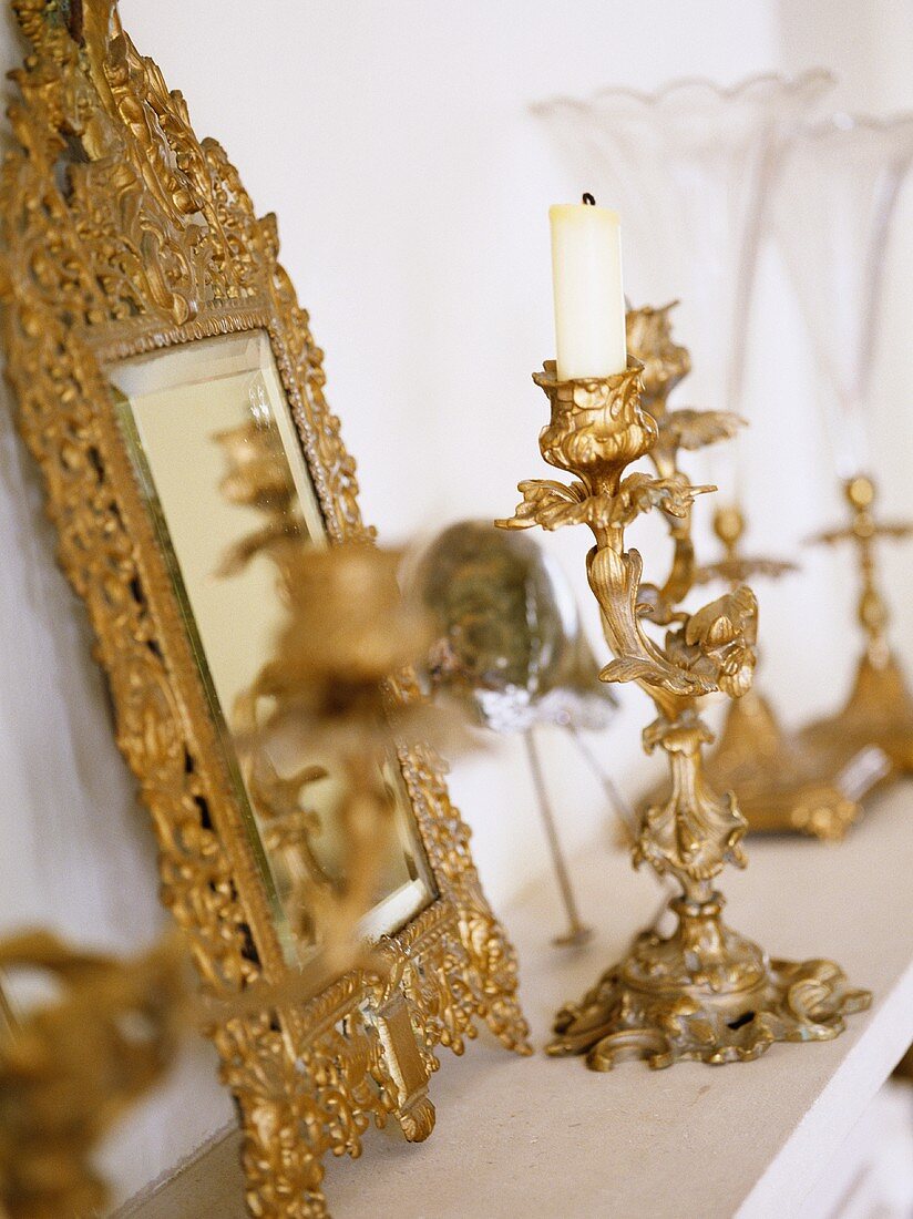 Close up of ornate gold framed mirror and candlesticks on mantelpiece.