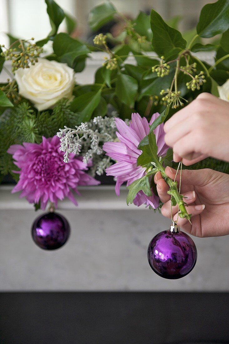 Violette Weihnachtskugel von Hand gehalten vor Blumengesteck