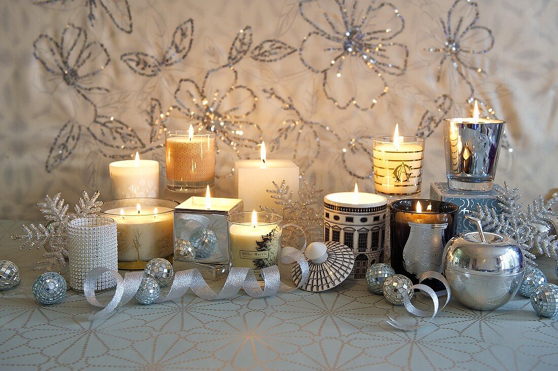 Brennende Kerzen in verschiedenen Glasgefässen auf festlich dekorierter Ablage