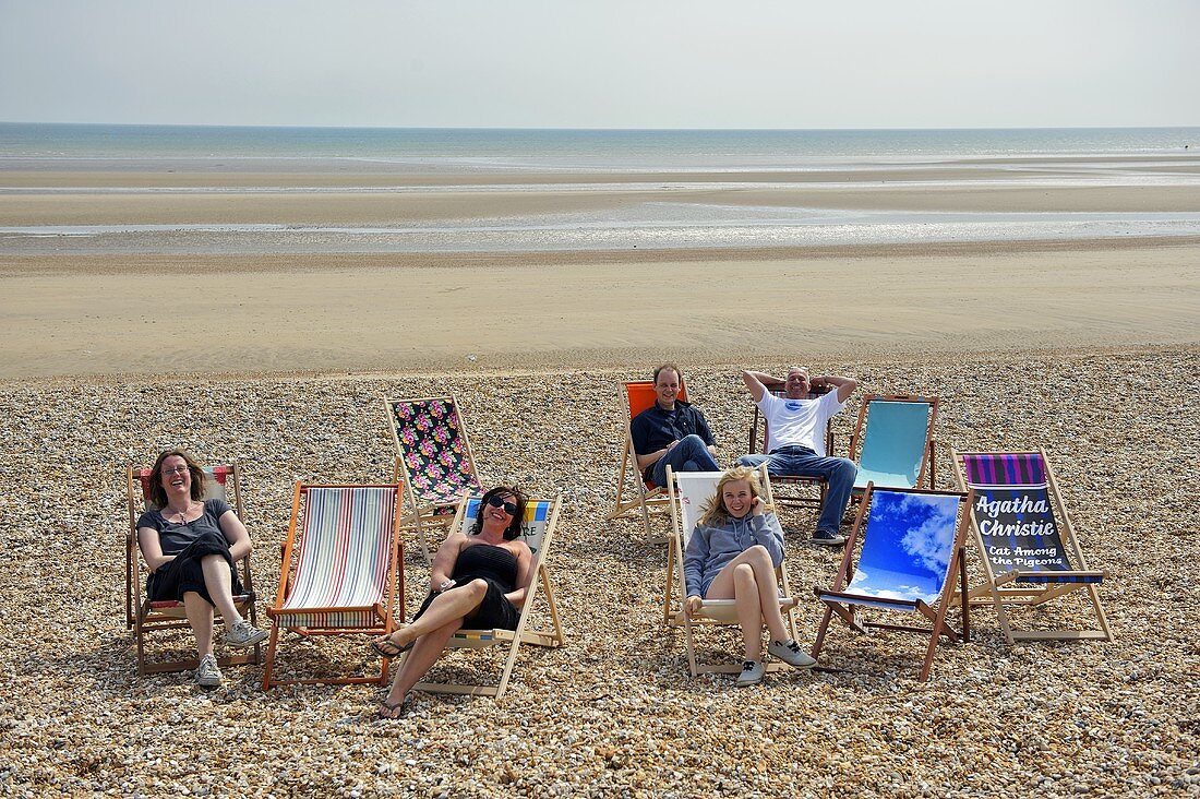 Frauen und Männer in Liegestühlen am Strand mit Meerblick