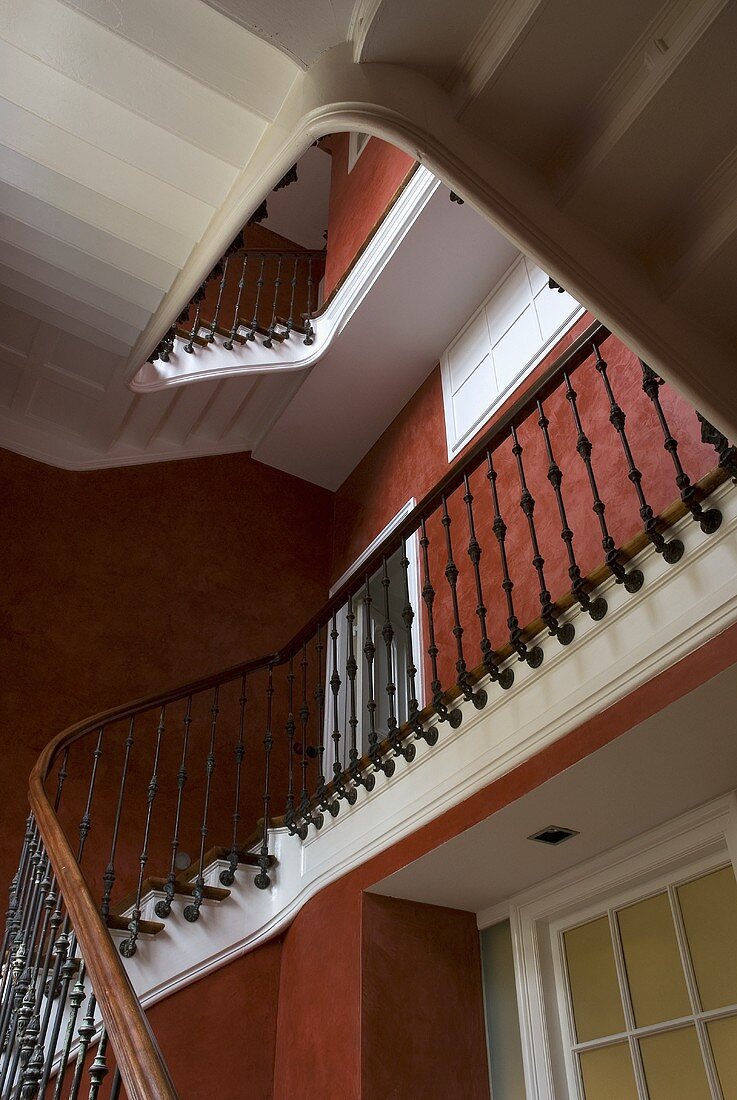 A white stairway with a wooden banister and red-brown sponge-painted walls