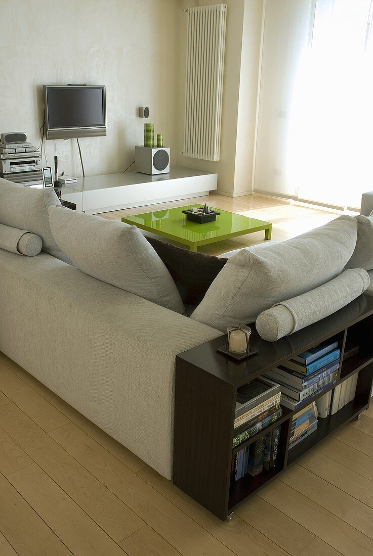 A low wooden shelf behind an light-coloured corner sofa