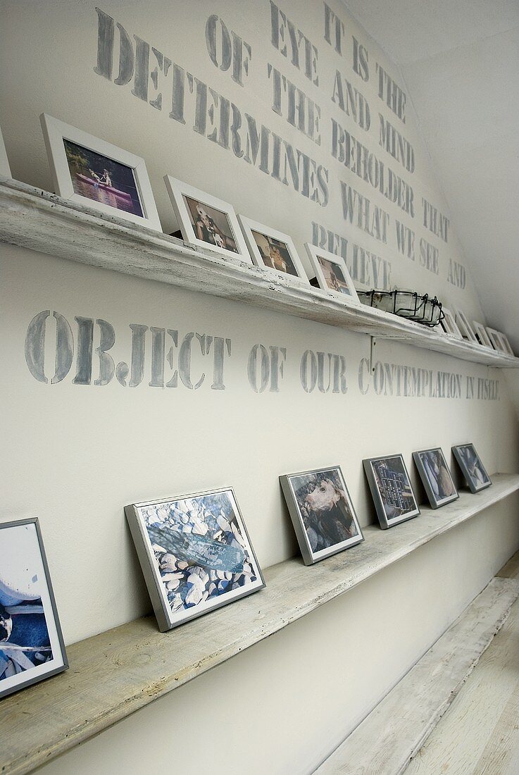 weiße Ablage mit Photosammlung vor beschrifteter Wand