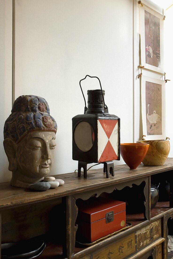 A Buddha head next to an old lantern on an antique sideboard