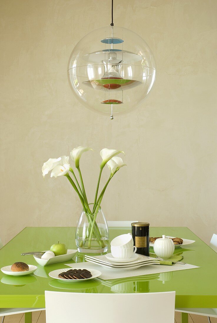 Designer pendant light above a green dining table set for breakfast