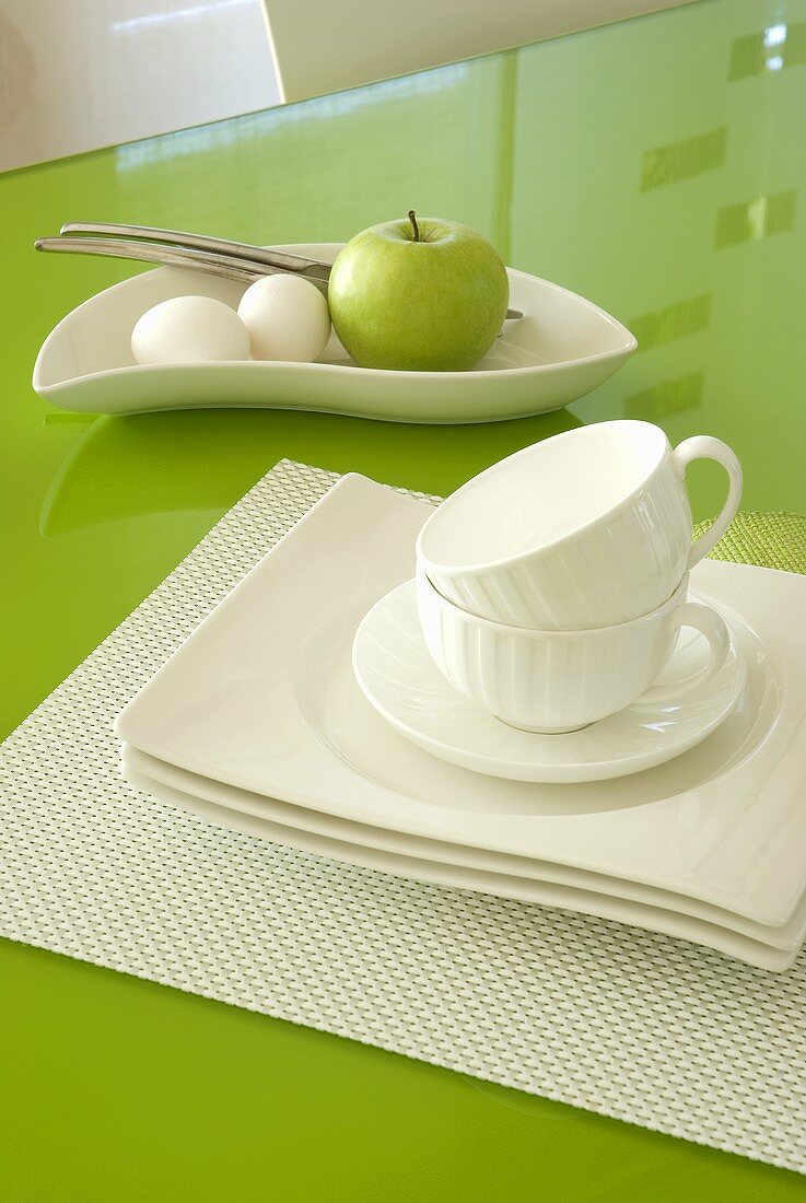 Weisses Frühstücksgedeck auf grünem Tisch aus Glas