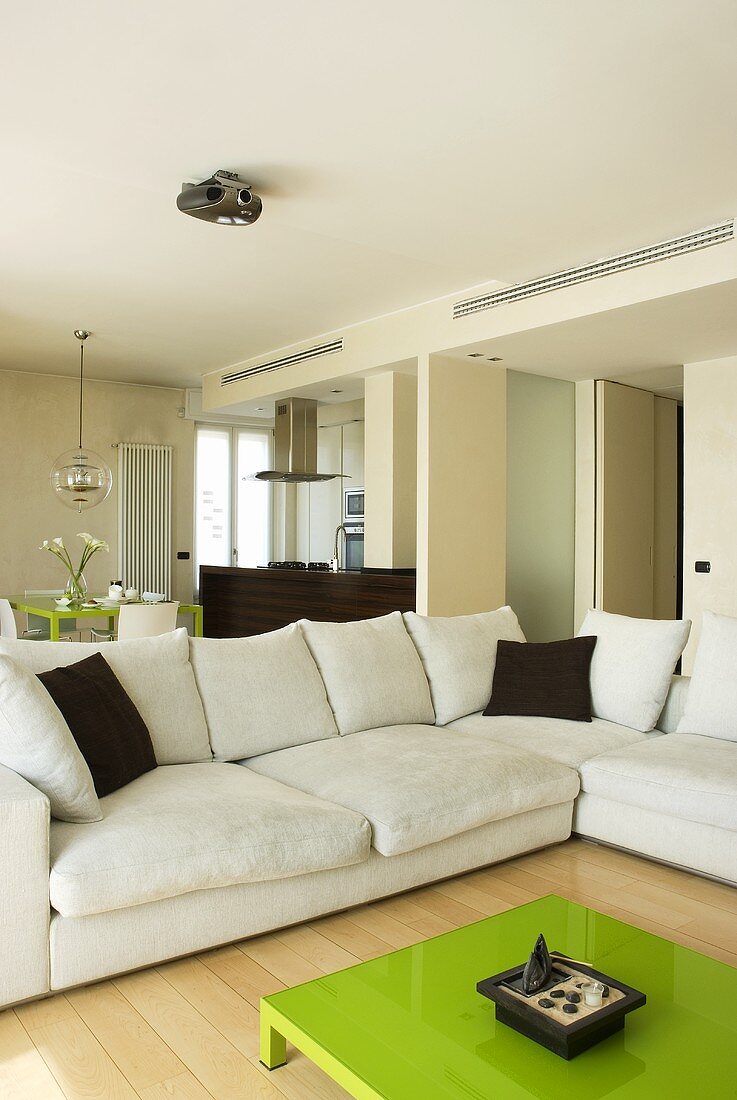Grüner Couchtisch vor weißem Sofa übereck mit braunen Kissen im offenen Wohn- und Essbereich
