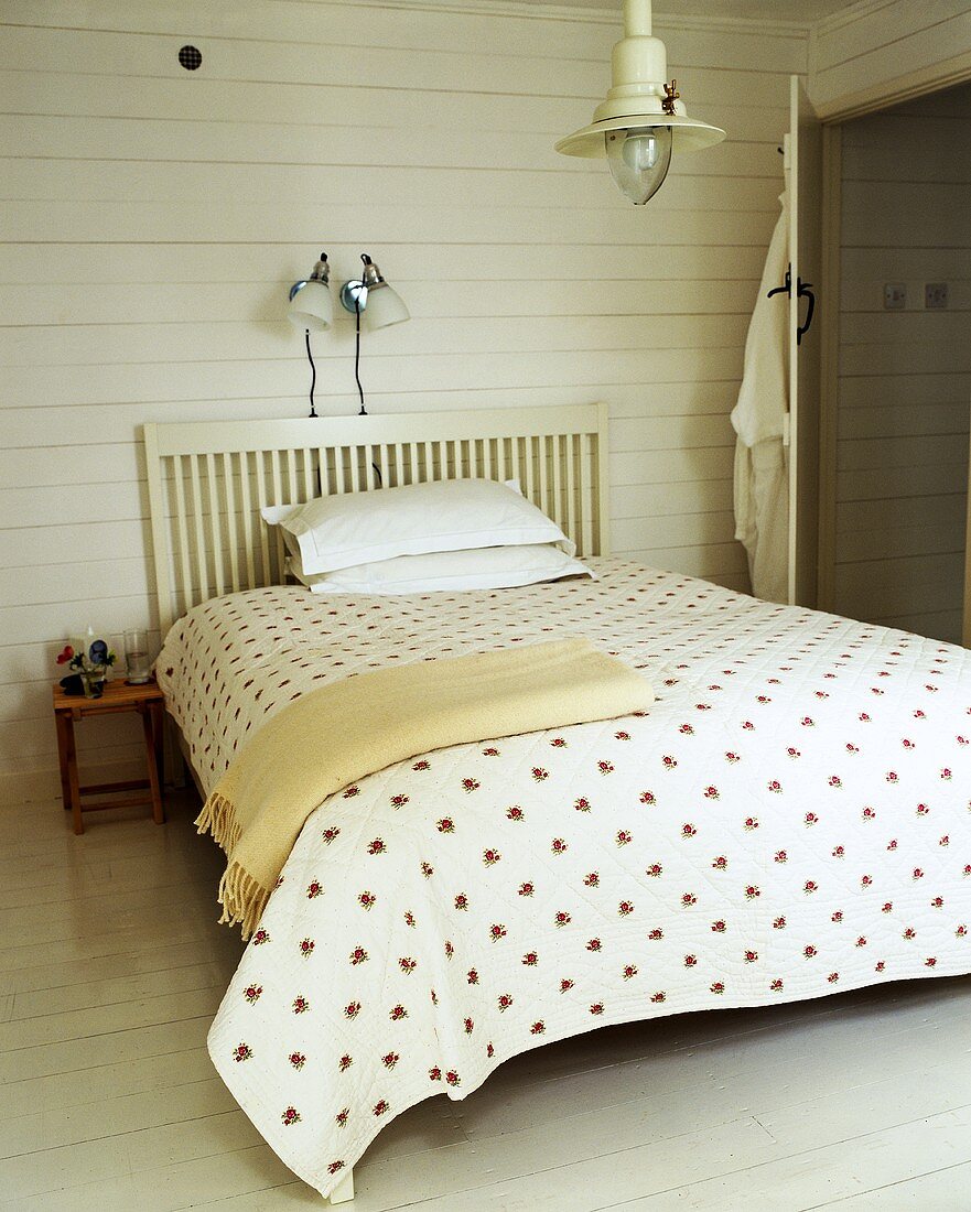 A bed in a country house with a wooden, slated headboard against a white wooden wall