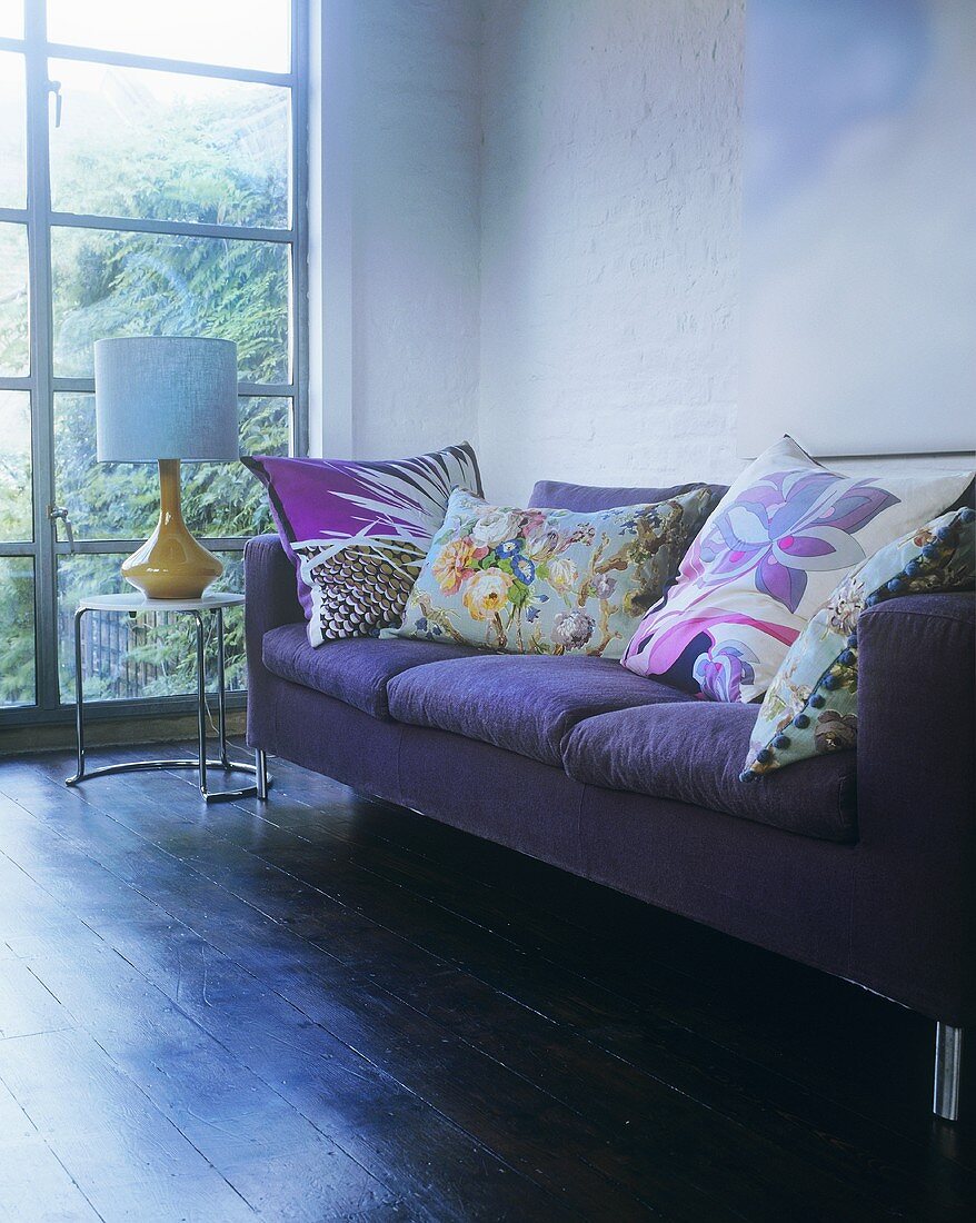 Violettes Sofa mit Kissen neben Fenster