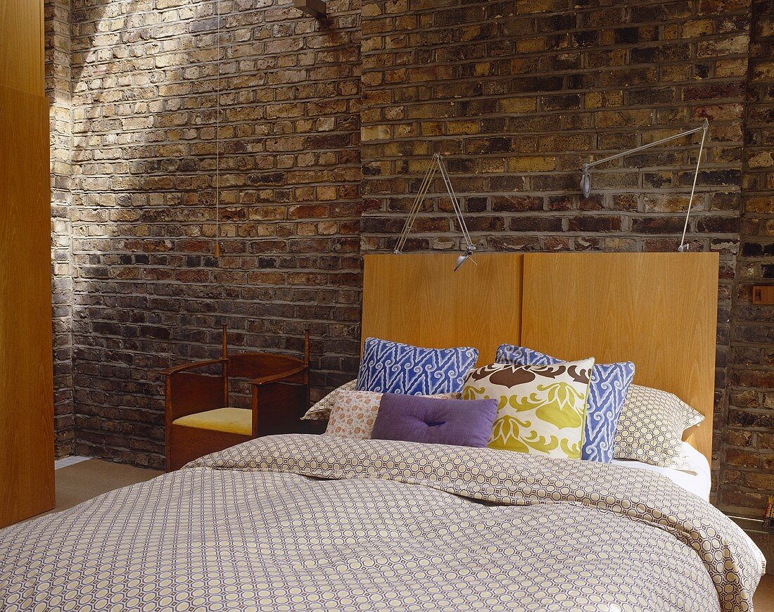 Double bed with wood headboard in front of a brick wall