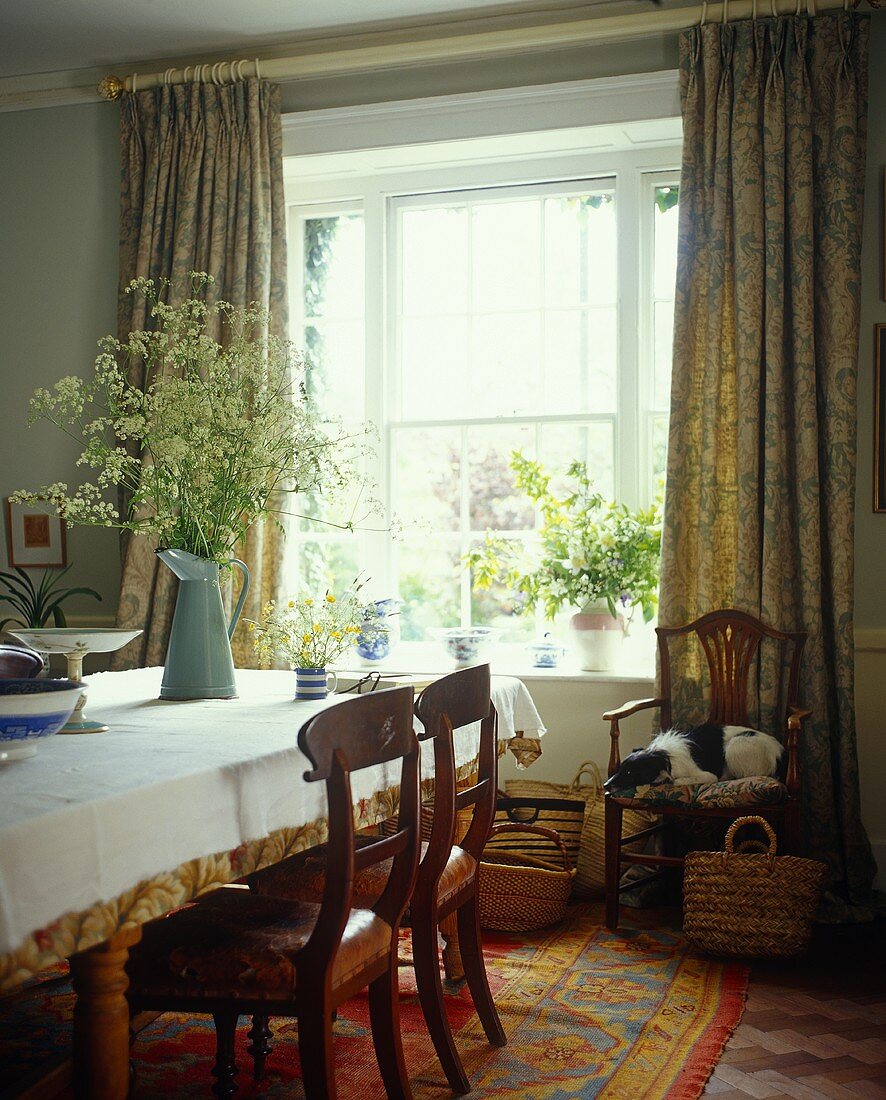 A traditional dining room with a window and floor-length curtains