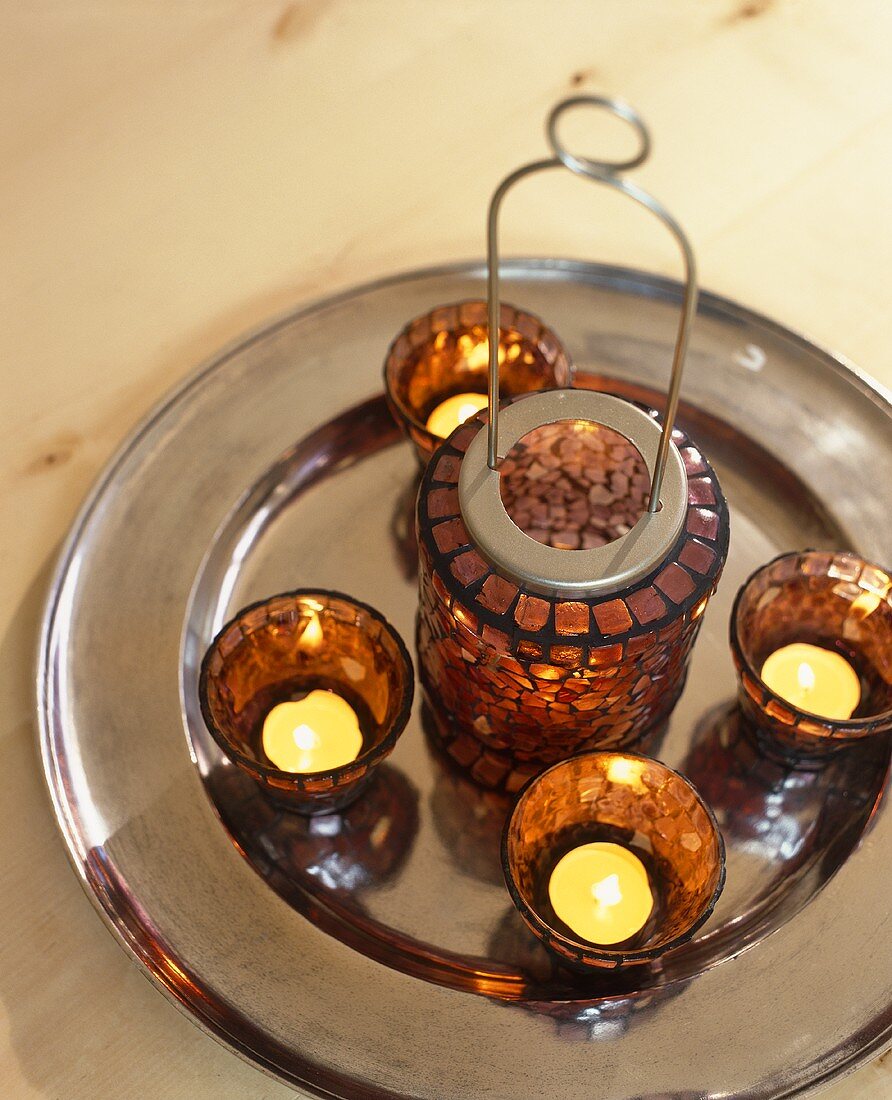 Tea light in a brown glass holders and lantern on a silver platter