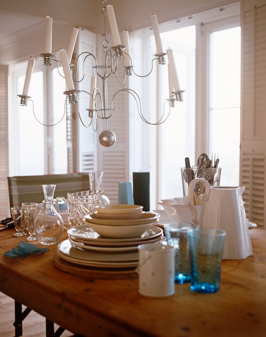 A chandelier with white candles above a wooden table set with crockery