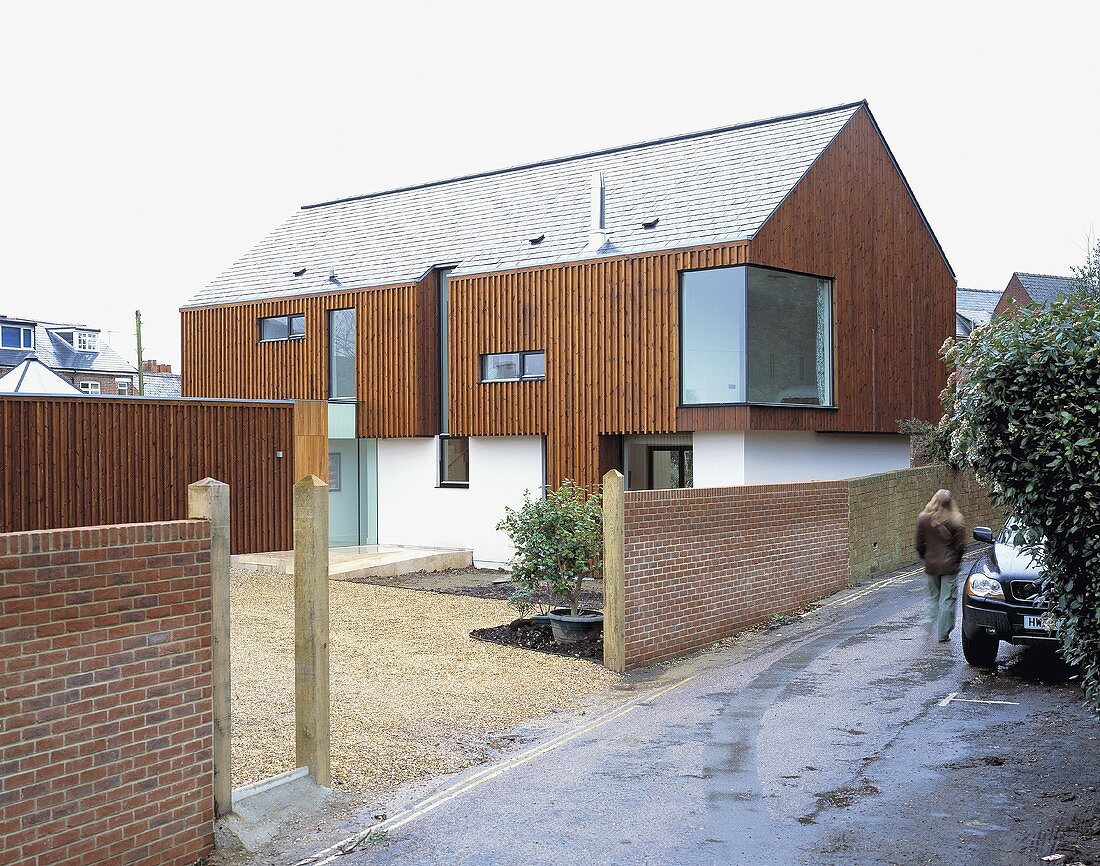 A new house built partially using wood panelling with a brick wall around the property