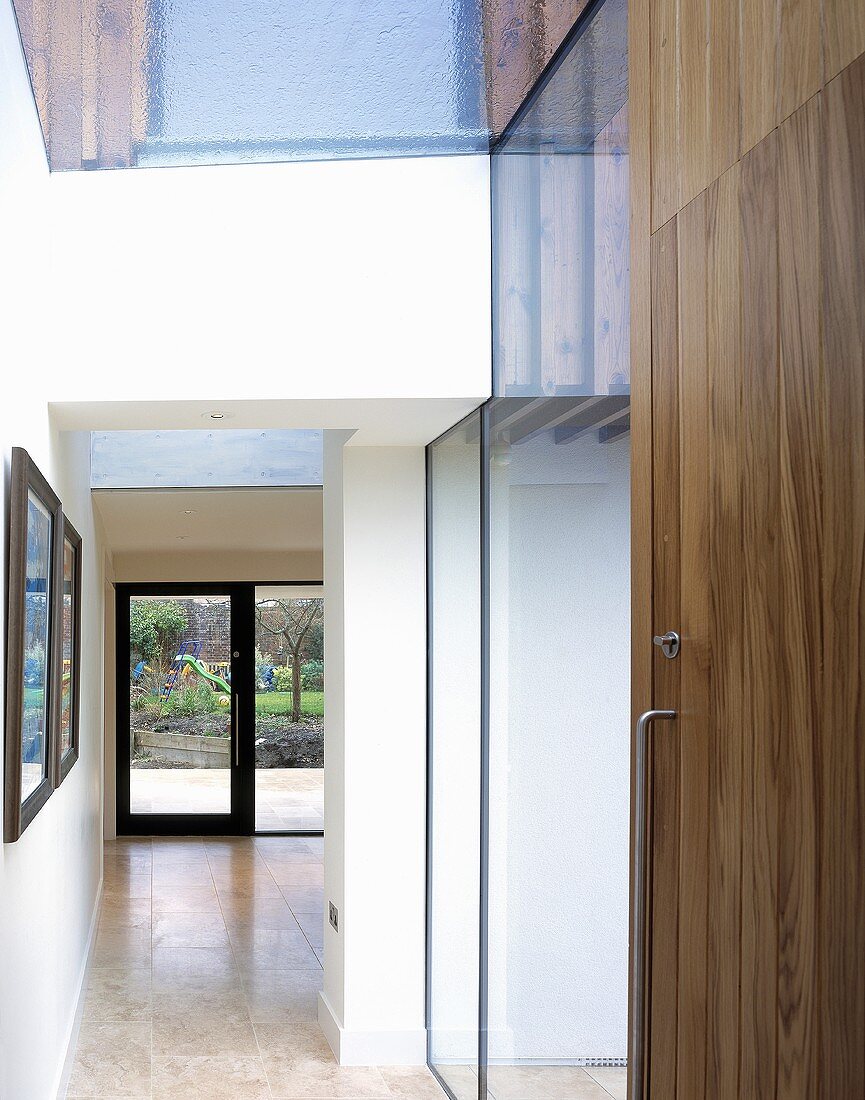 A hallway with a wooden, built-in cupboard and a view into an open room to the terrace door