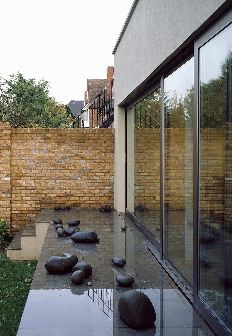 Glänzender Terrassenboden mit Dekosteinen vor Haus und Ziegelwand