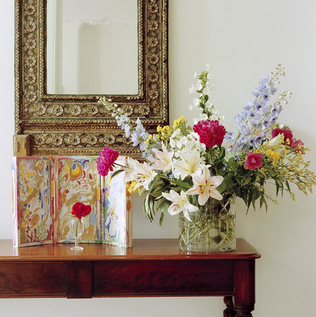 Wandtisch mit Sommerstrauss und Bild, darüber Spiegel mit verziertem Rahmen