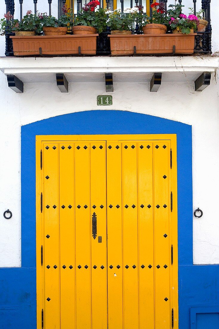 Gelbe Haustür mit blauem Türrahmen, darüber Blumenkästen