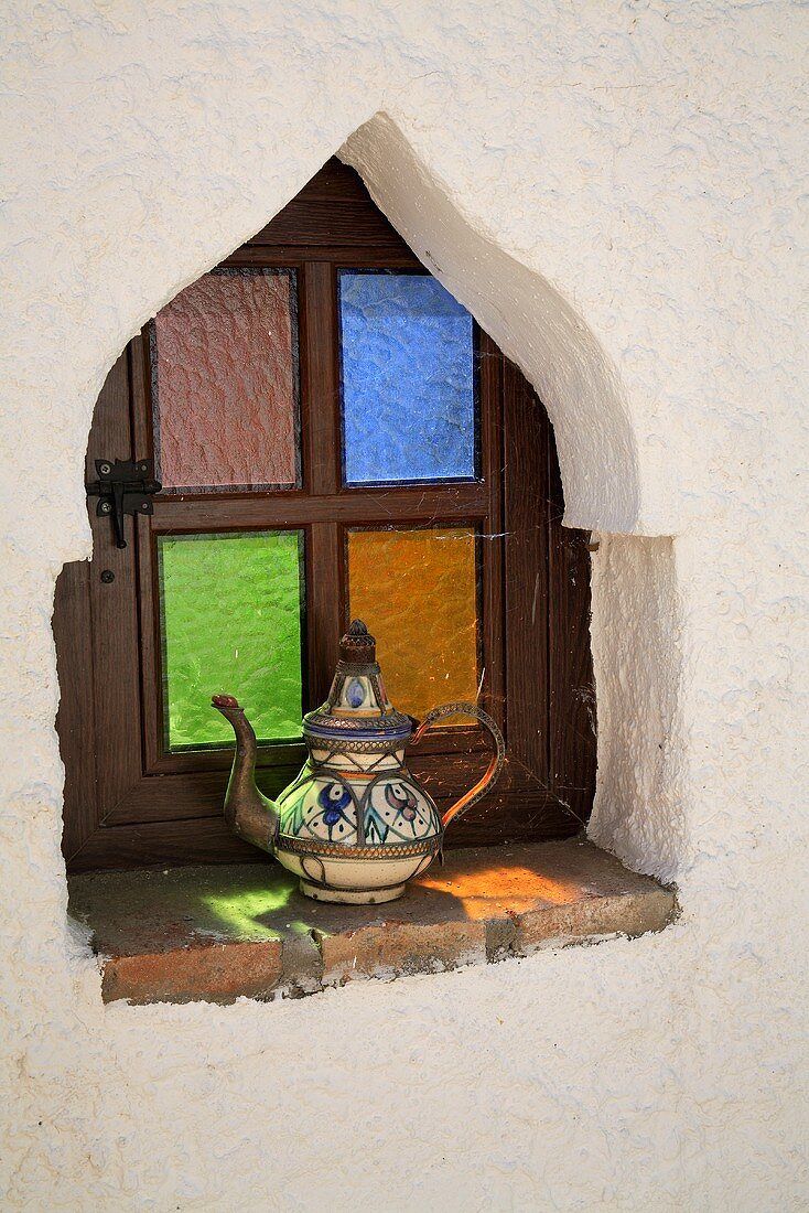 Keramik Kaffeekanne auf Fensterbank eines maurischen Fensters mit bunten Gläsern