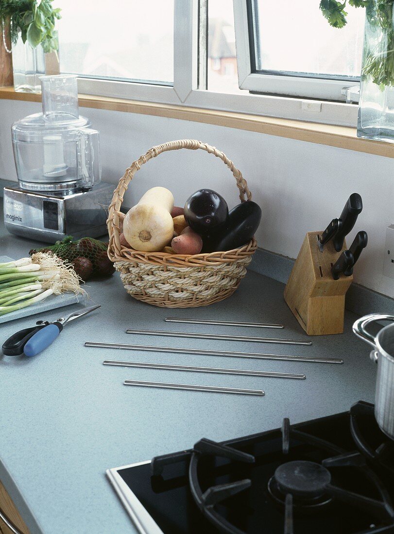 Korb mit Gemüse neben Messerblock auf grauer Küchenarbeitsplatte