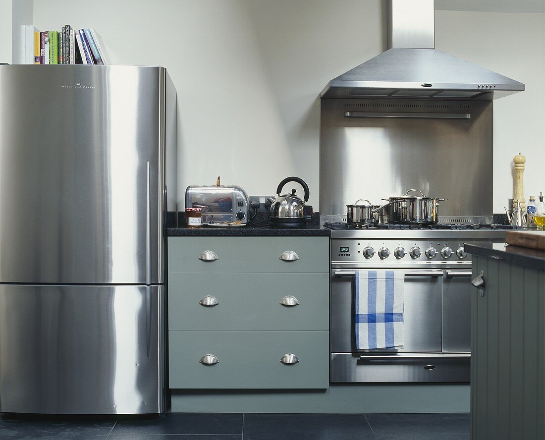 Kühlschrank und Küchenofen aus Edelstahl neben Küchenunterschrank mit grauer Holzfront