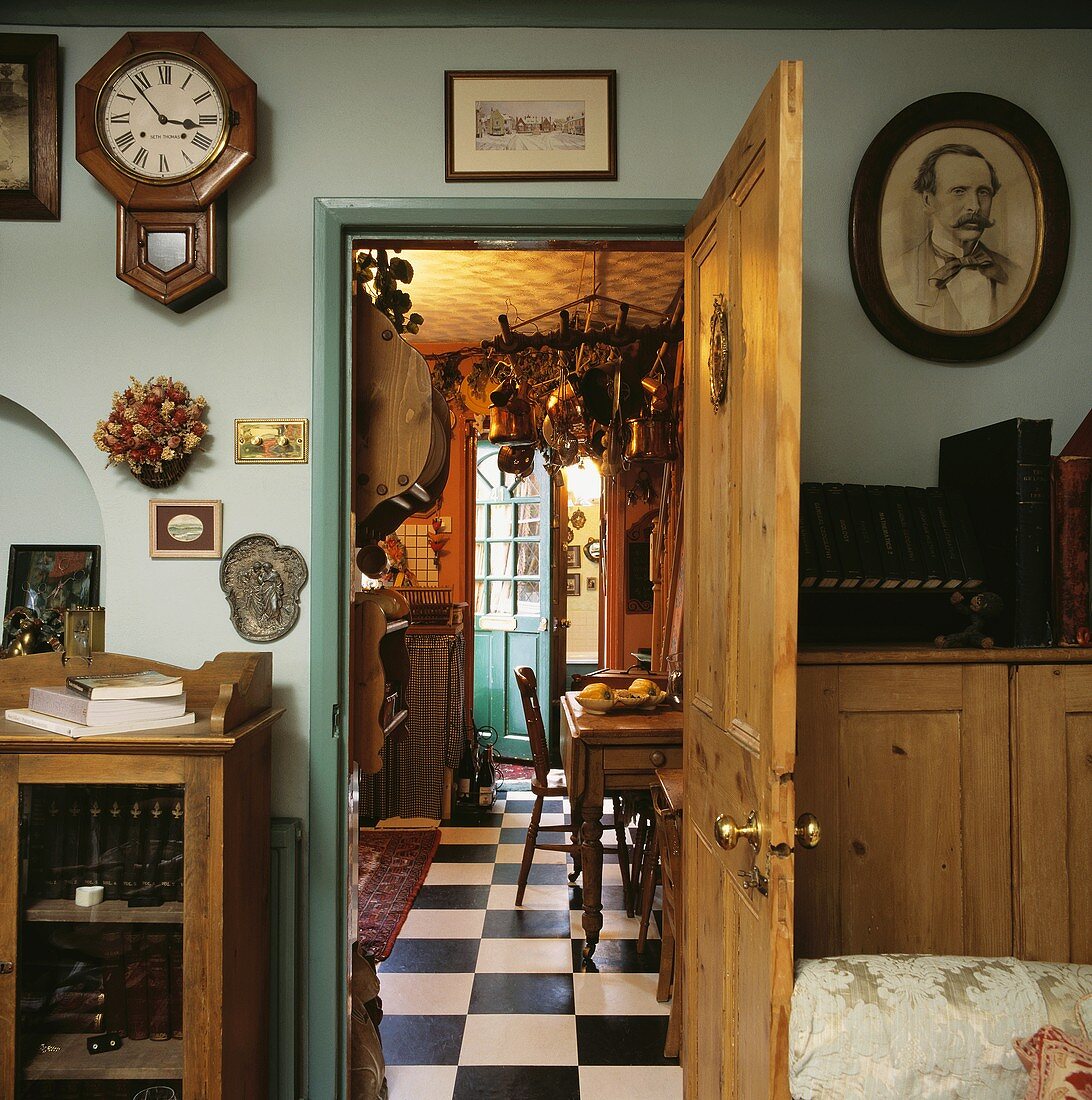 Offene Holztür mit darüber hängender Wanduhr, öffnet den Blick zu einer traditionellen Küche mit schwarz-weiss gefliestem Fußboden