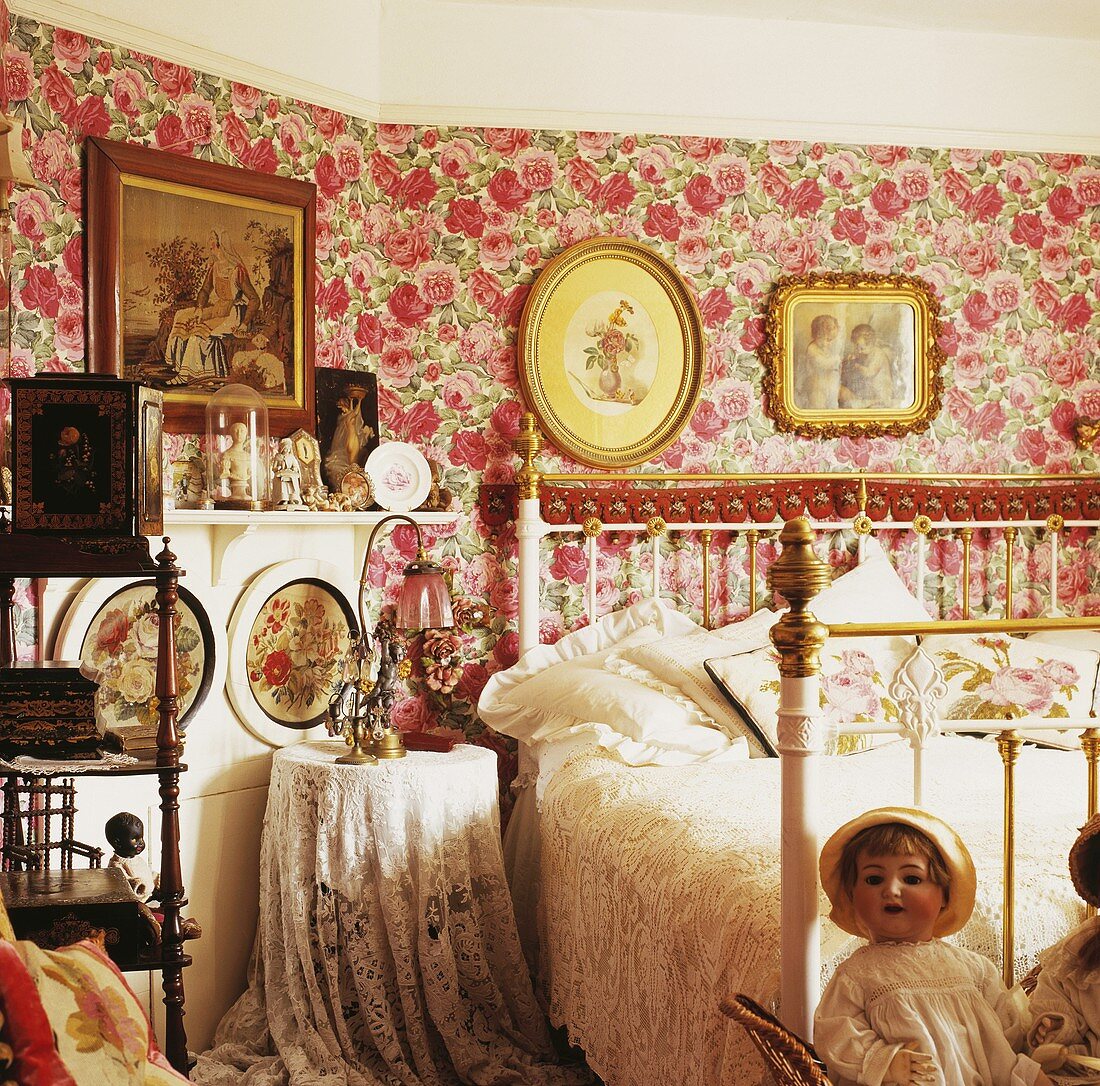 Viktorianisches Schlafzimmer mit einer rosa Rosen-Tapete, einem antiken weissen Messing und Eisen-Bett und mit einer Glaslampe und Puppen