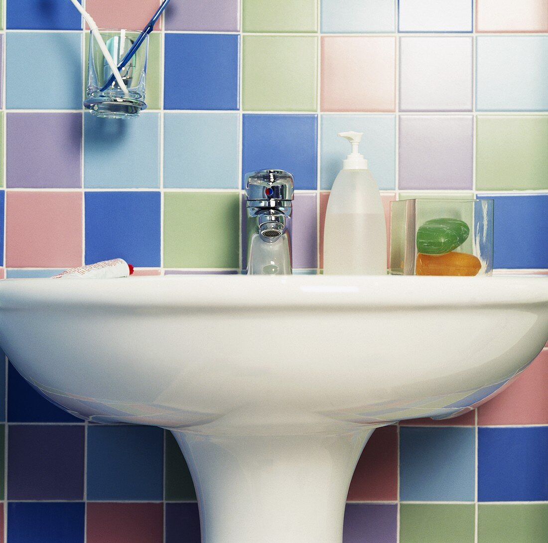 Nahaufnahme von Toilettenartikeln auf einem weißen Waschbecken, rundherum bunte, pastellfarbene Wandfliesen
