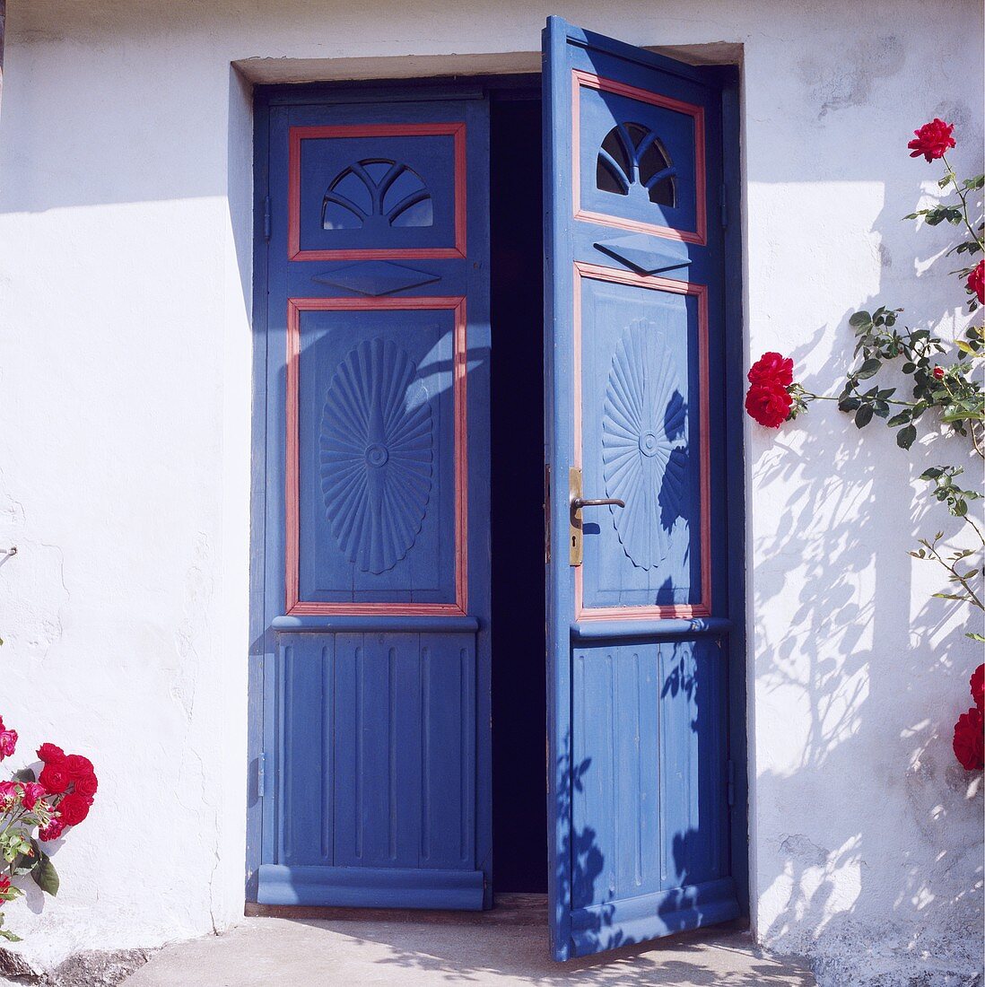 Weisses Landhäuschen mit blauer Doppeltür und Kletterrosen