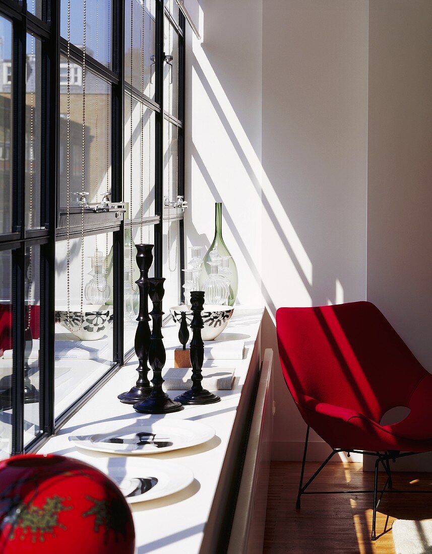 A set of black candle sticks on a window sill and a red Bauhaus-style armchair