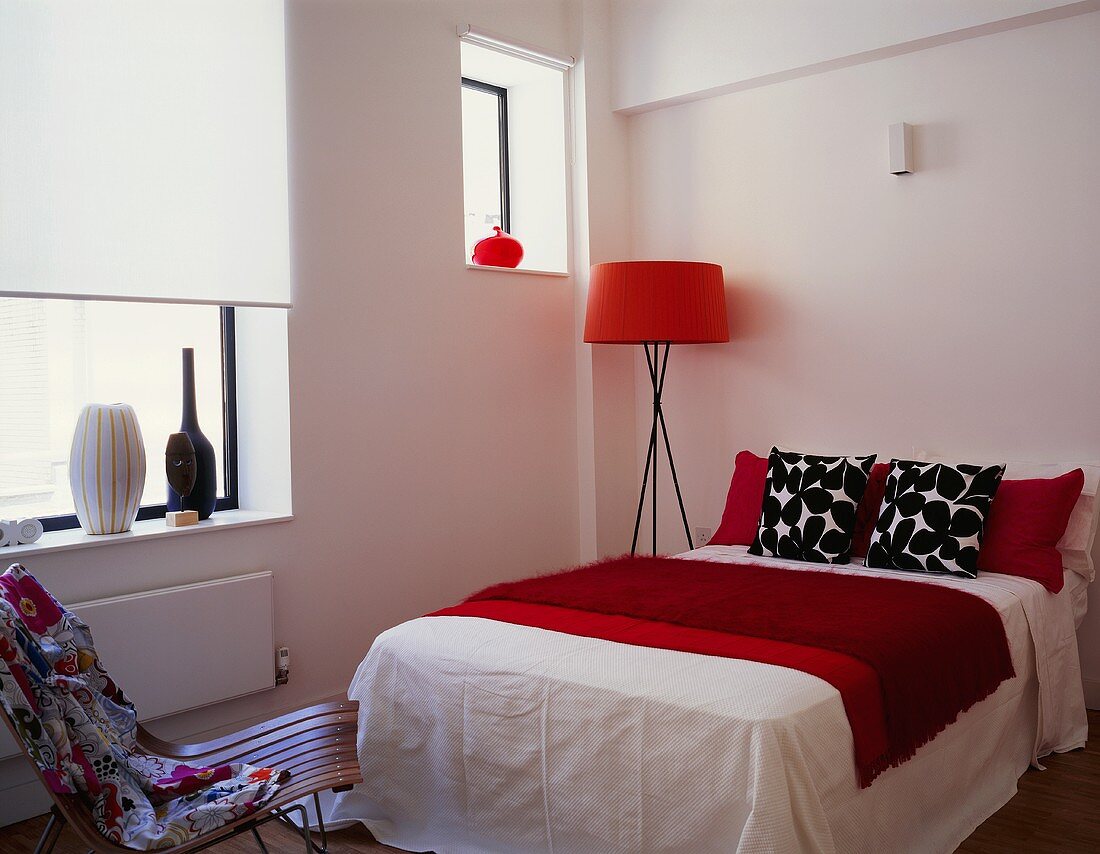 Stehlampe mit rotem Schirm neben Doppelbett mit schwarz weißem Kissen und roter Tagesdecke