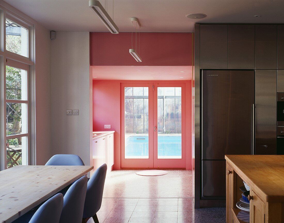 An open-plan kitchen with a dining area and a view through a doorway of a red glass door
