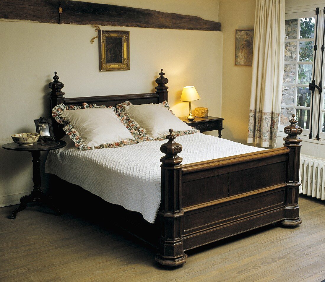 Antikes Mahagoni-Bett mit cremefarbener Bettdecke und Kissen in einem Landhaus- Schlafzimmer