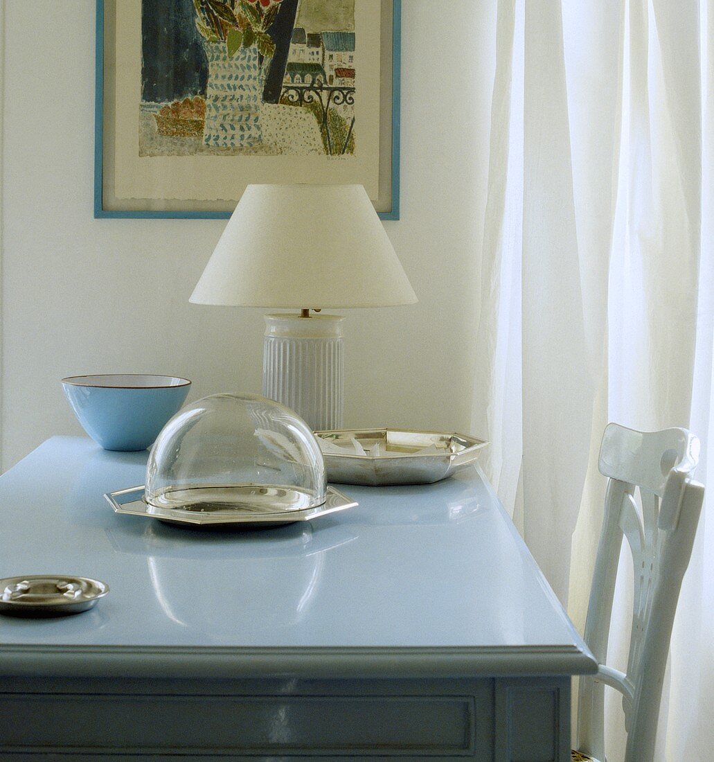 Glas-Cloche und weiße Lampe auf pastellblauem Tisch