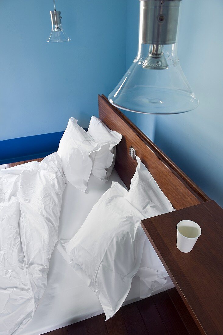 Blick von Oben auf Hotelbett mit weisser Bettwäsche, Ablage aus Holz & Deckenleuchten aus Glas