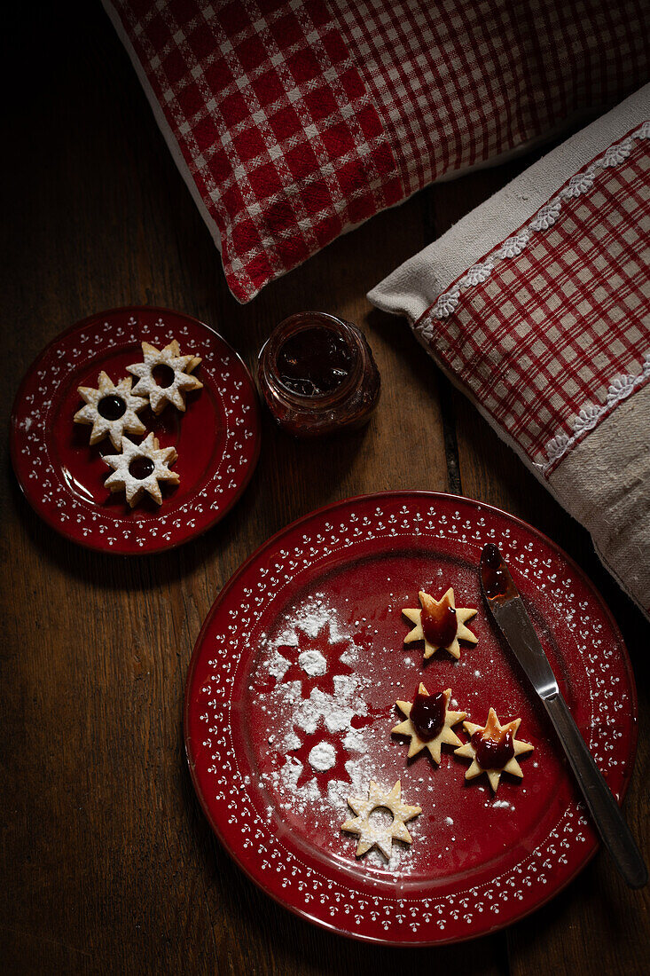 Weihnachtsplätzchen (Spitzbuben) mit Marmelade und Messer, rote Teller, auf Holzuntergrund