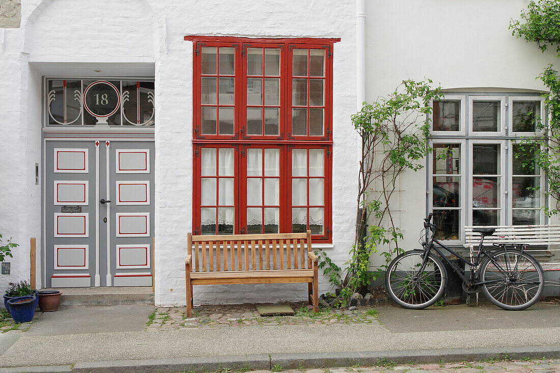 Alte Haustür und Sprossenfenster, davor eine Sitzbank und ein Fahrrad