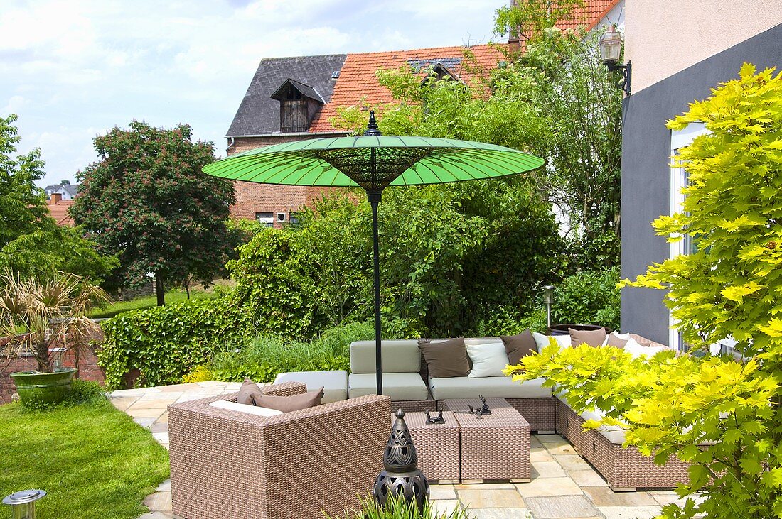 Korbmöbel auf Terrasse am Haus mit grünem Sonnenschirm
