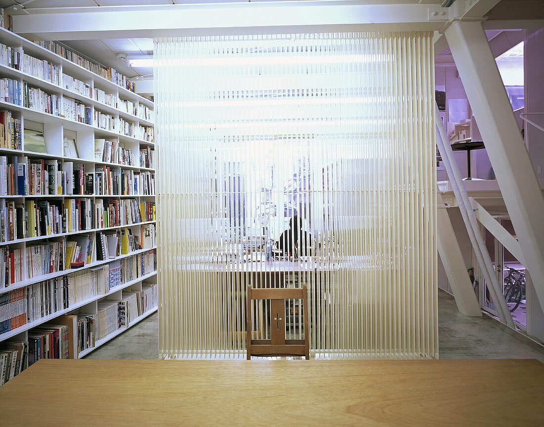 An office with a transparent room divider and a built-in bookshelf