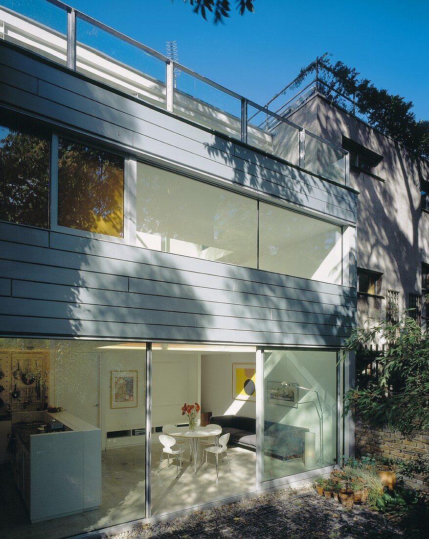 Fassade eines Neubauhauses mit Fensterband und Blick durch offene Terrassentür in Wohnraum