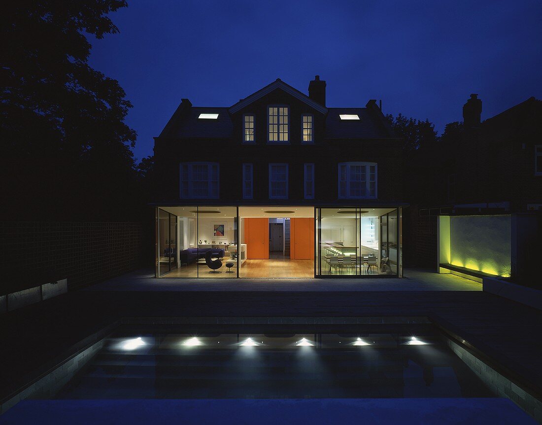A night view of a house with an illuminated, open-plan living room