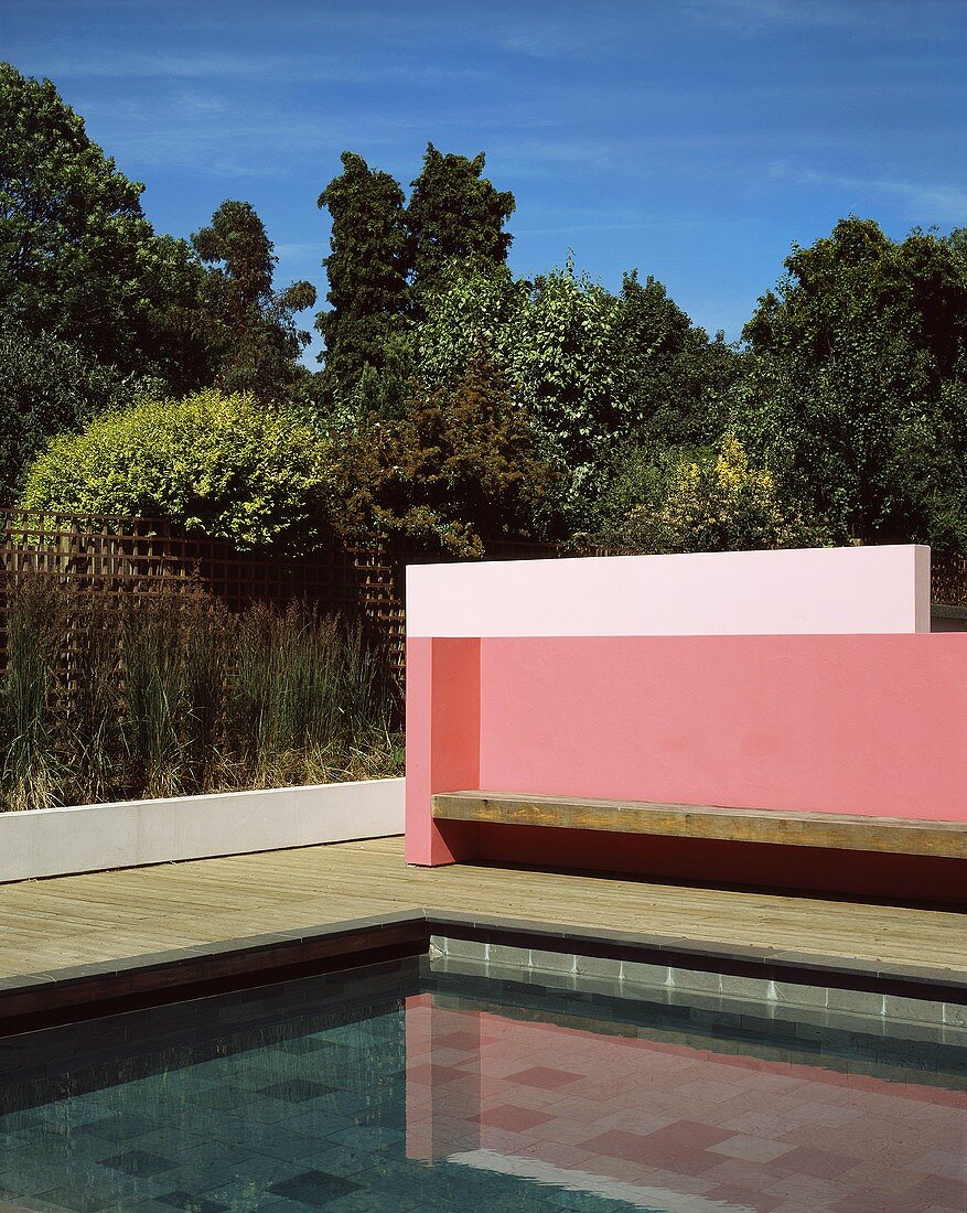 Eckenausschnitt einer modernen pinkfarbenen Wand mit Holzbank vor Pool