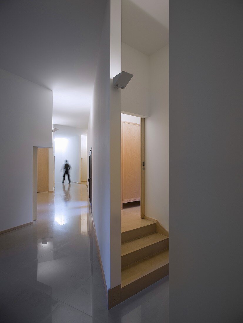 Puristischer Vorraum mit hochglänzendem Fliesenboden und Blick auf Treppenaufgang hinter Trennwand