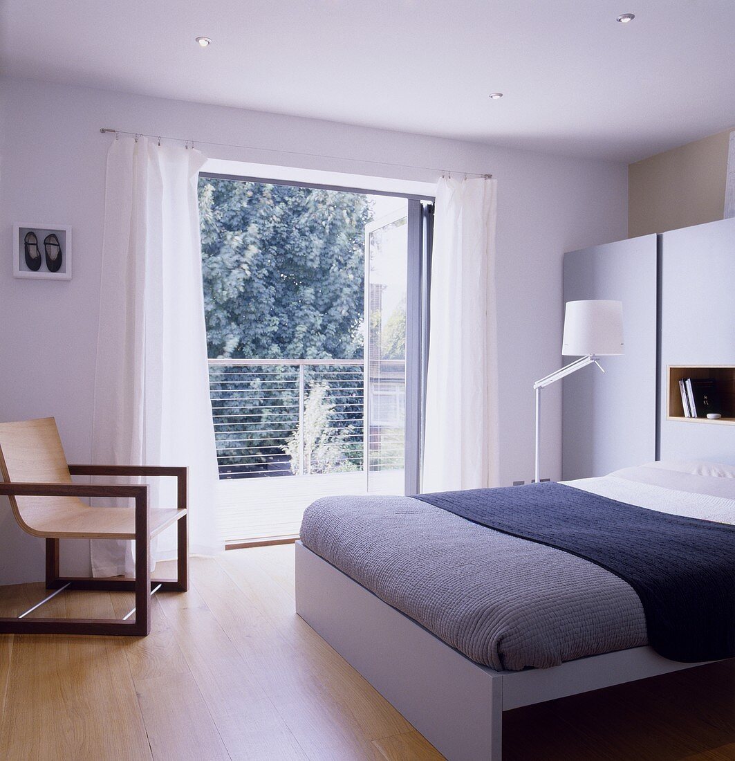 A modern bedroom with a double bed and an armchair next to an open balcony door