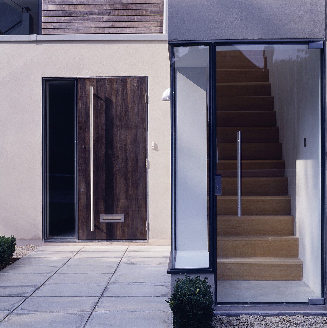 Verglaster Hauseingang eines modernen Wohnhauses mit Blick auf Treppenaufgang und zusätzliche Eingangstür aus Holz