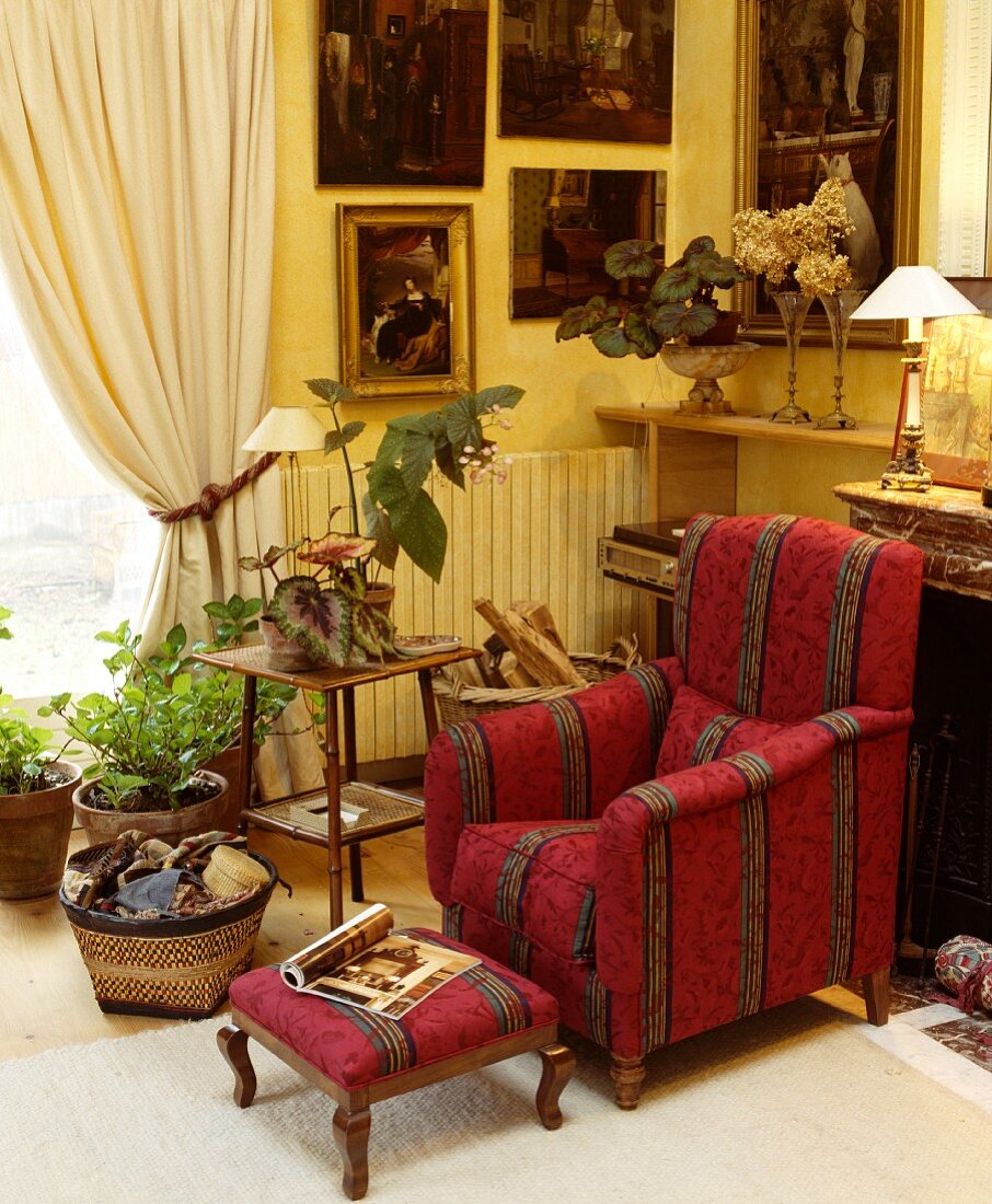 Gestreifter, roter Sessel mit passender Fussbank in traditionellem Wohnzimmer mit dunklen Gemälden auf pastellgelber Wand