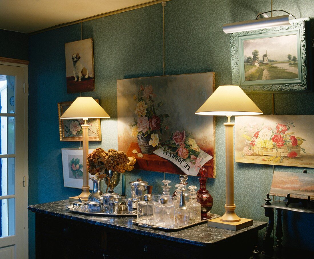 Brennende Lampen und antike Karaffen auf Marmorplatte vor Gemäldesammlung an blauer Wand