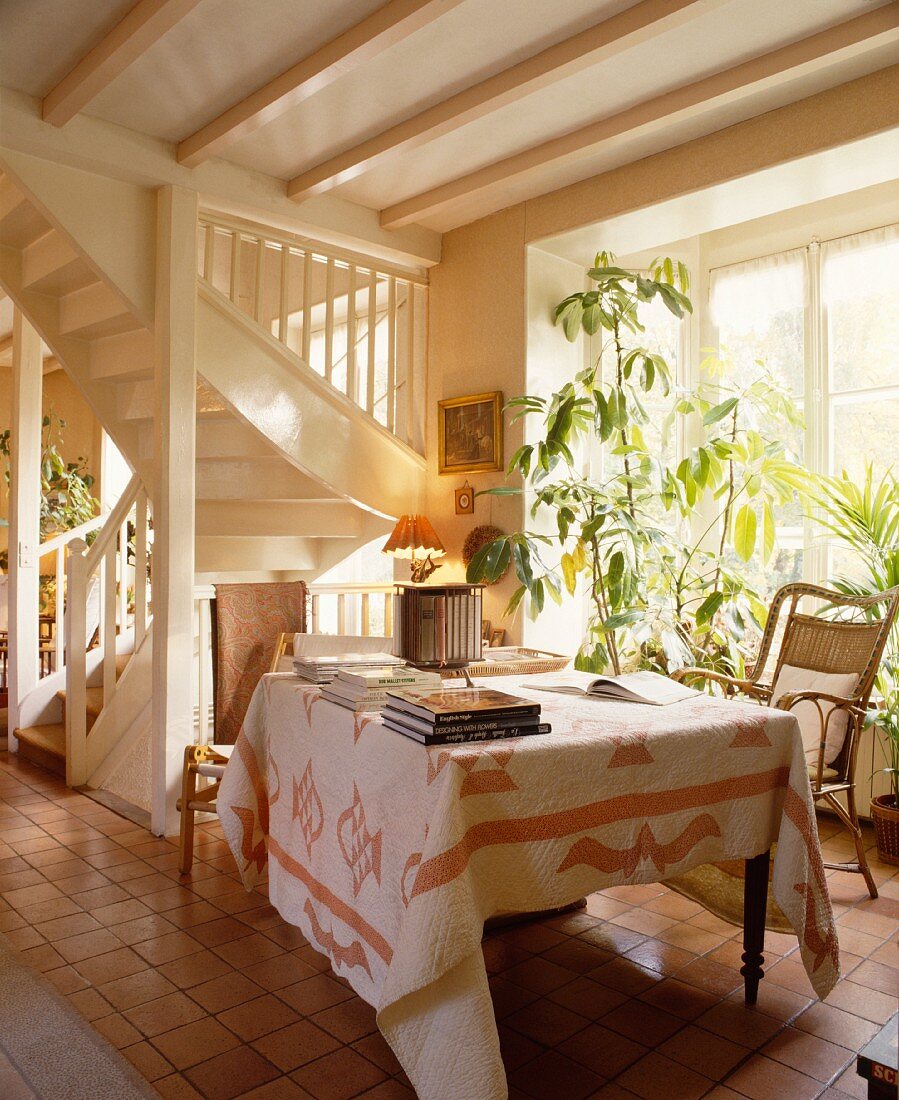 Patchwork-Decke auf Tisch vor weisser Holztreppe in Landhaus-Wohnzimmer