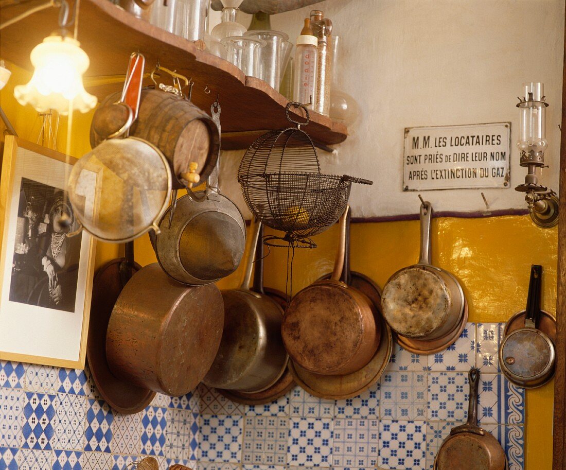 Alte Metallsiebe, Kupferpfannen und altes Emailleschild an Wand über blau-weissen Fliesen in französischer Küche