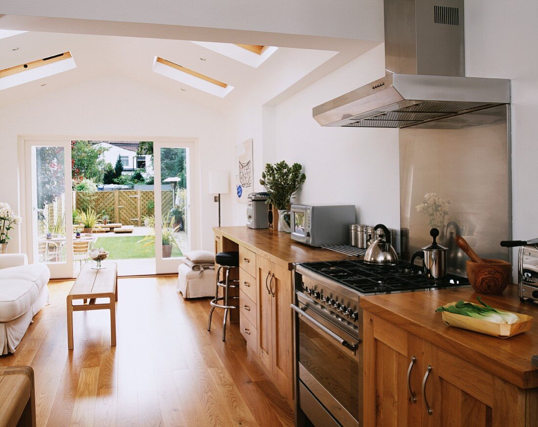 Küchenzeile aus Holz mit Edelstahl-Kocheinheit in offenem, modernem Wohnraum mit Blick in den Garten